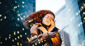 Mulher em pé, em uma cidade, olhando o celular com o semblante de preocupação