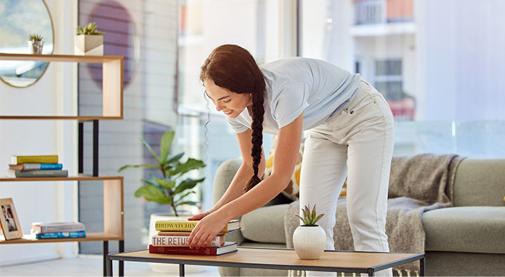 Mulher arrumando alguns livros na mesa da sala e sorrindo